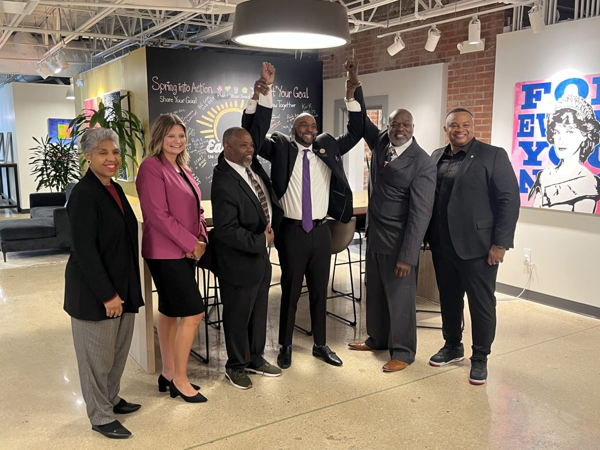 A group of people hold up their hands in celebration while wearing suits