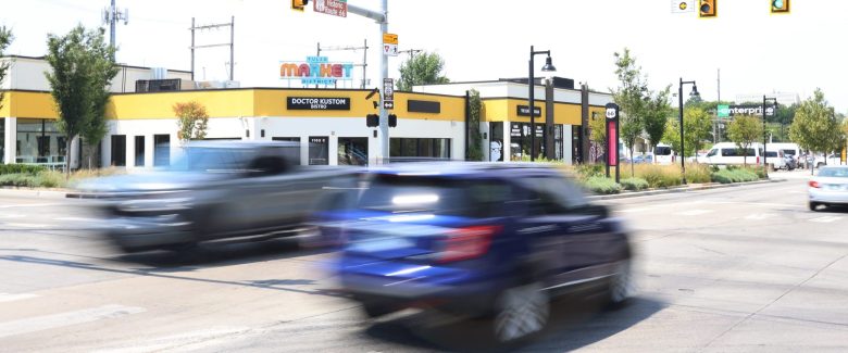 A blue car streaks by on the road in front of a building
