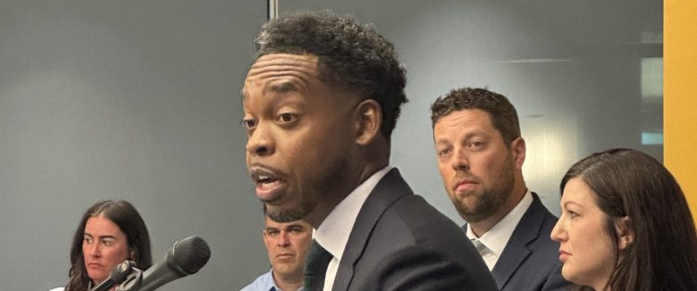 A man in a suit stands behind a mic.