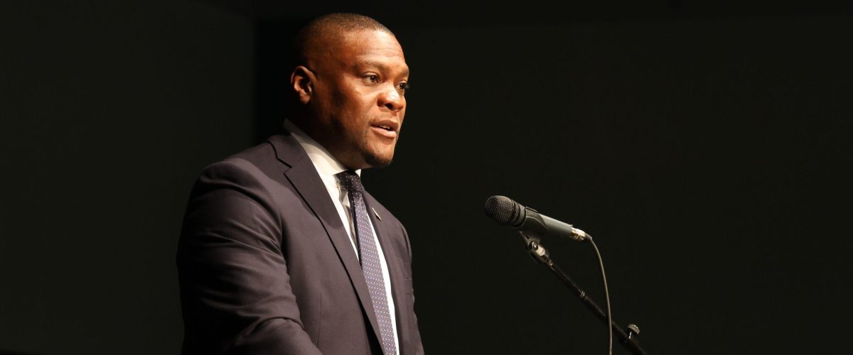 A man in a suit stands at a podium in an auditorium.