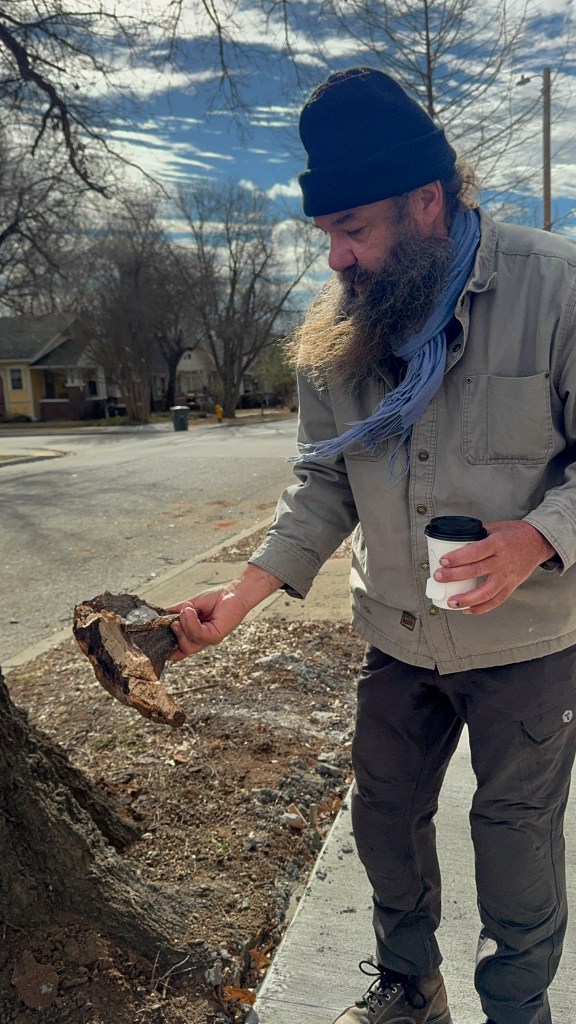 Man holds at tree root while holding cup of coffee