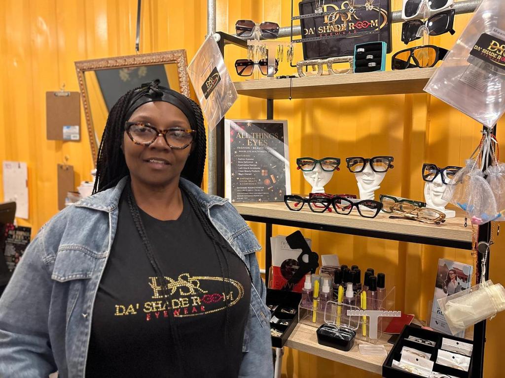 Rene’ Bramlett poses next to frames inside Da'Shade Room Eyewear in The Boxyard, Nov. 25, 2025. 