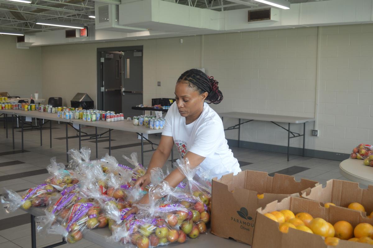 Stored Goodness founder Montoyria Jones places a bag of apples on a table at the organization's June 26, 2026, community market at O'Brien Park Recreation Center.