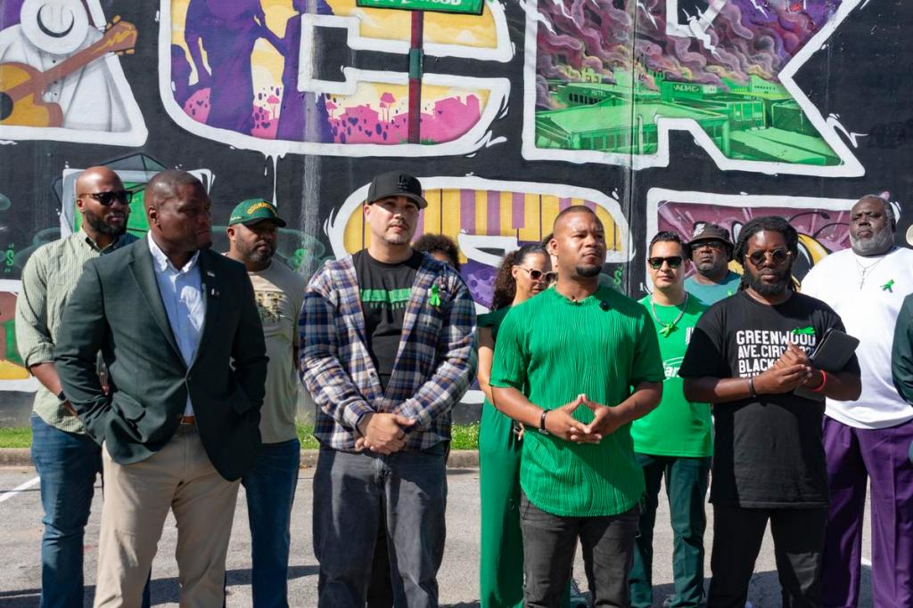 Tony Williams, second from front right, led a vigil near the Black Wall Street mural in Greenwood May 31, 2026. Mayor Monroe Nichols, front left, joined the group wearing "Green for Greenwood."